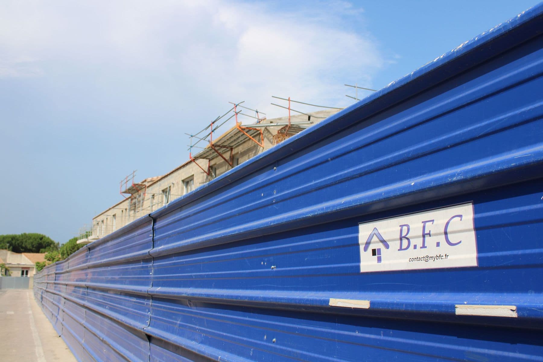 La palissade bleue du chantier portant l’enseigne BFC, la résidence en arrière-plan