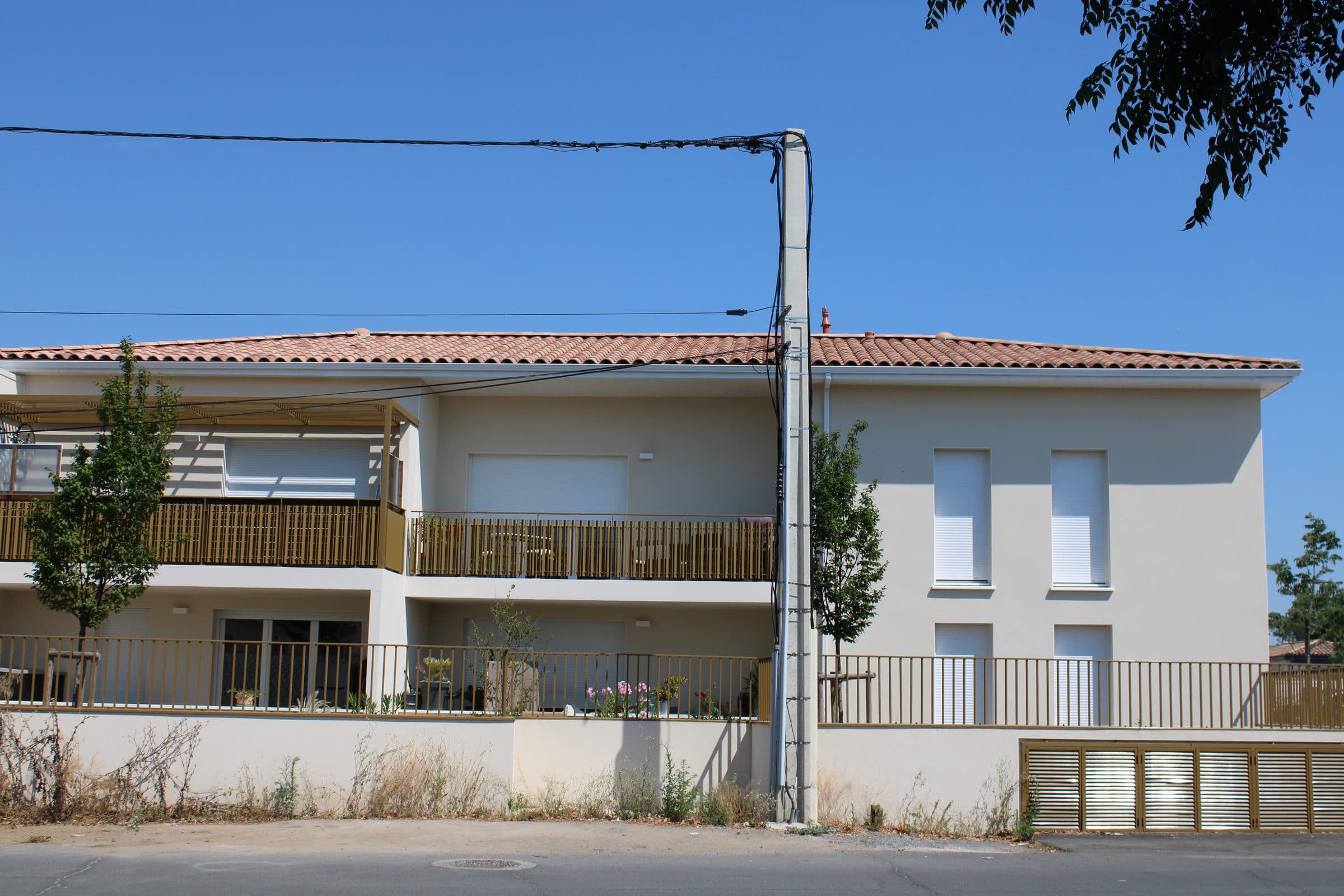 Façade sur rue de la Résidence L’Écrin d’O à Vias : balcons et garde-corps en bois, toiture en tuiles