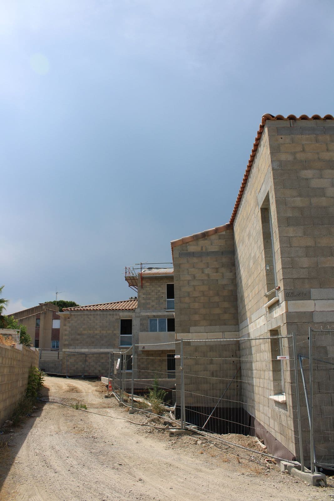 L’angle d’une aile en blocs béton, barrières de chantier et piste en terre
