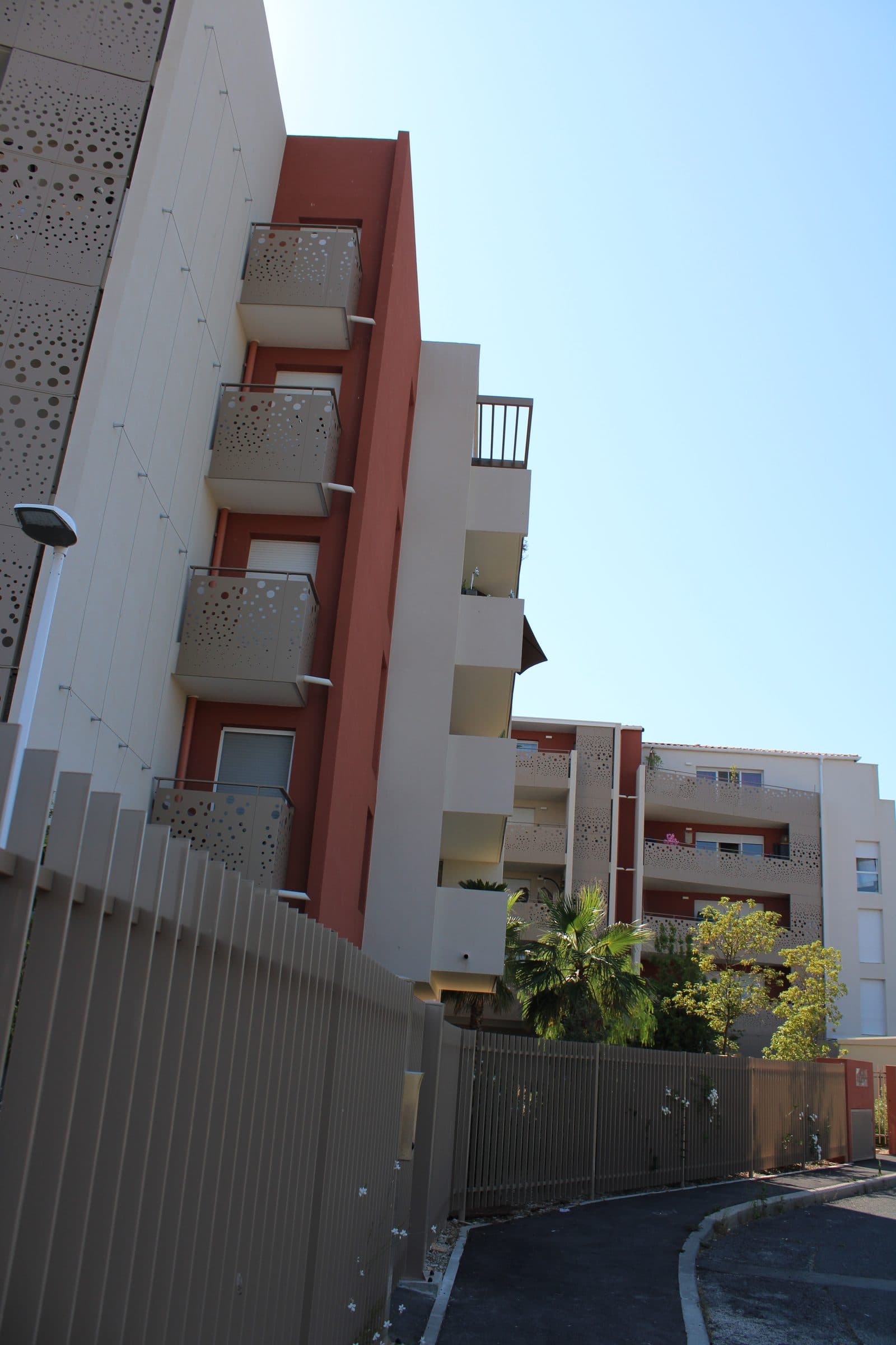 Pignon ocre rouge et balcons de la résidence, en contre-plongée depuis la rue