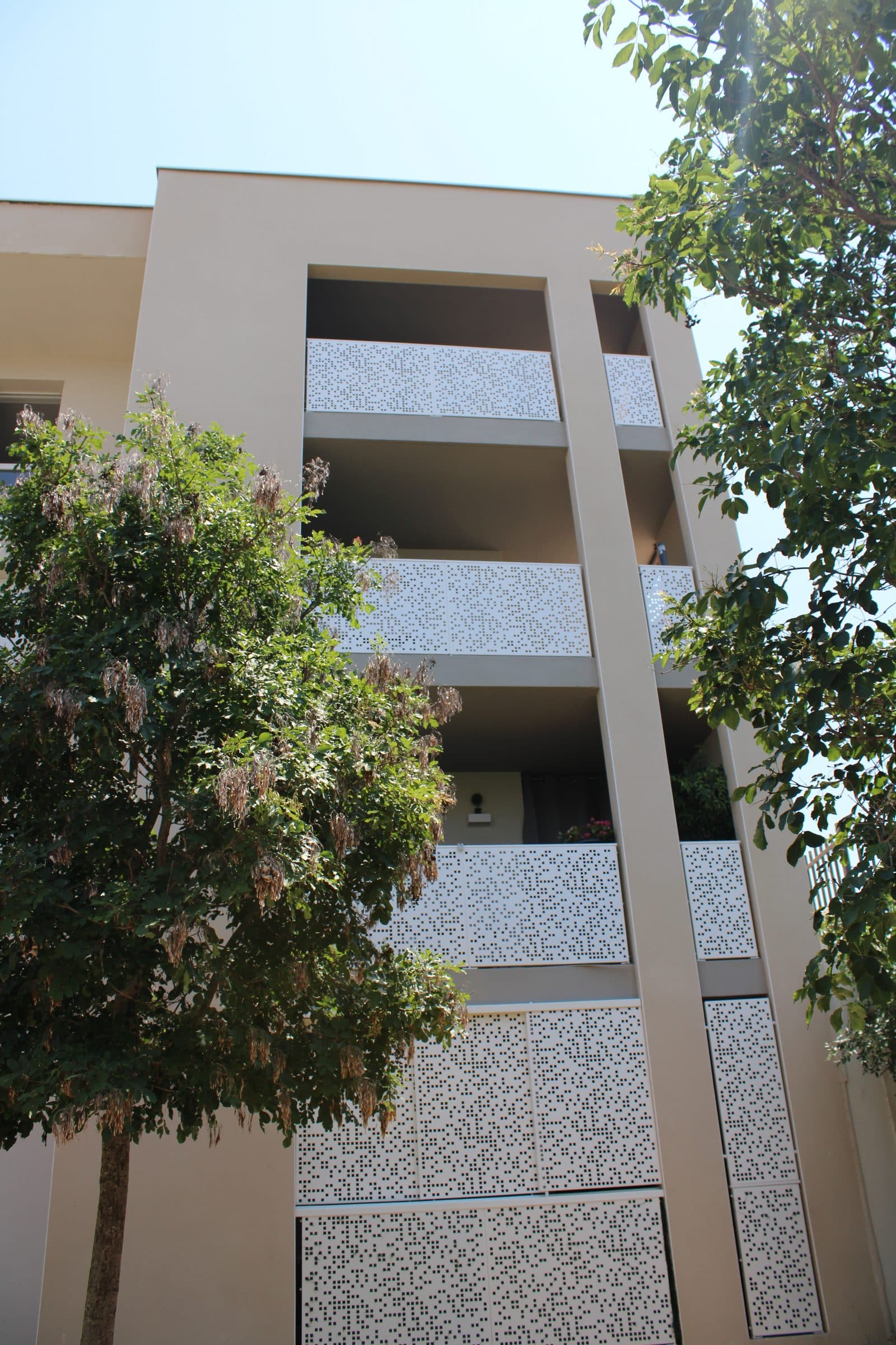 Balcons habillés de panneaux ajourés, derrière le feuillage d’un arbre