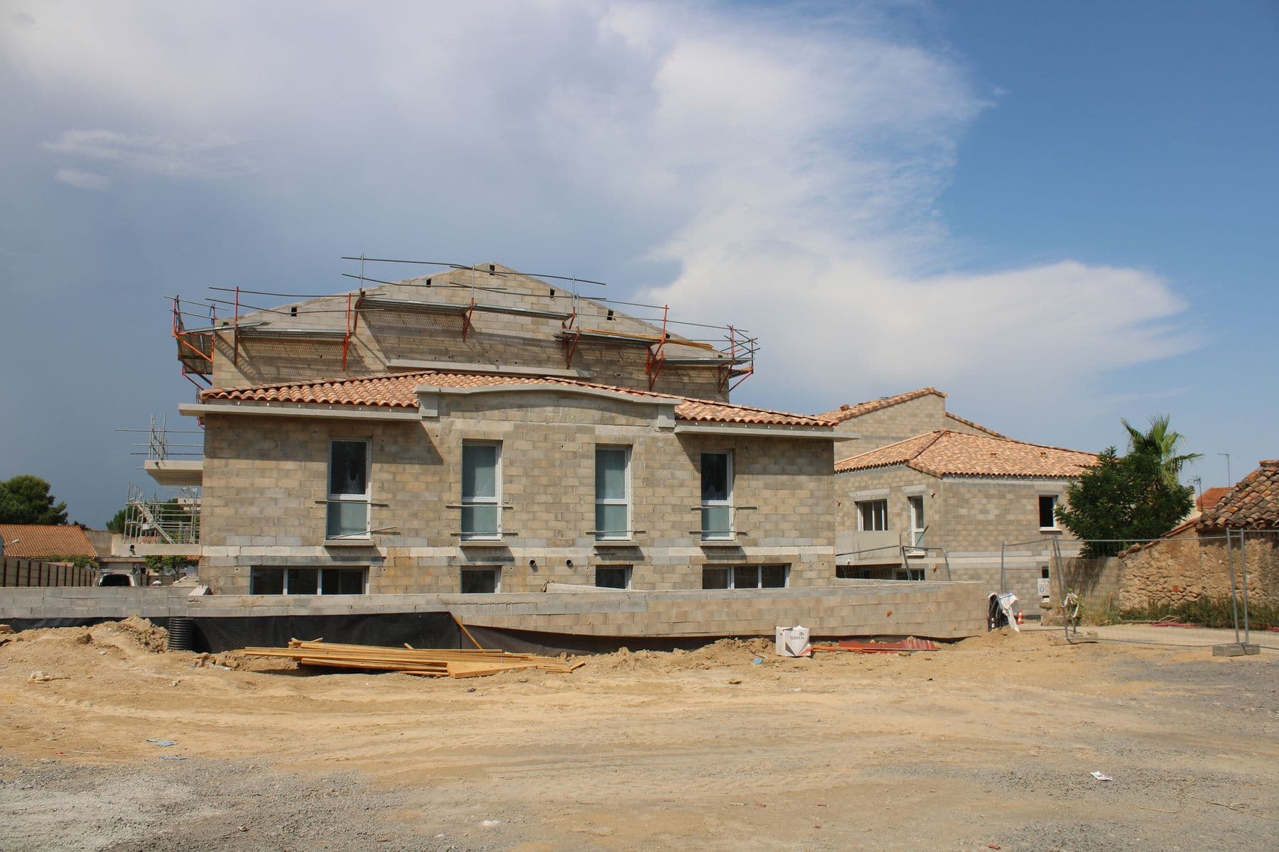 Le bâtiment en blocs béton sous un ciel chargé, plateforme encore en terre au premier plan