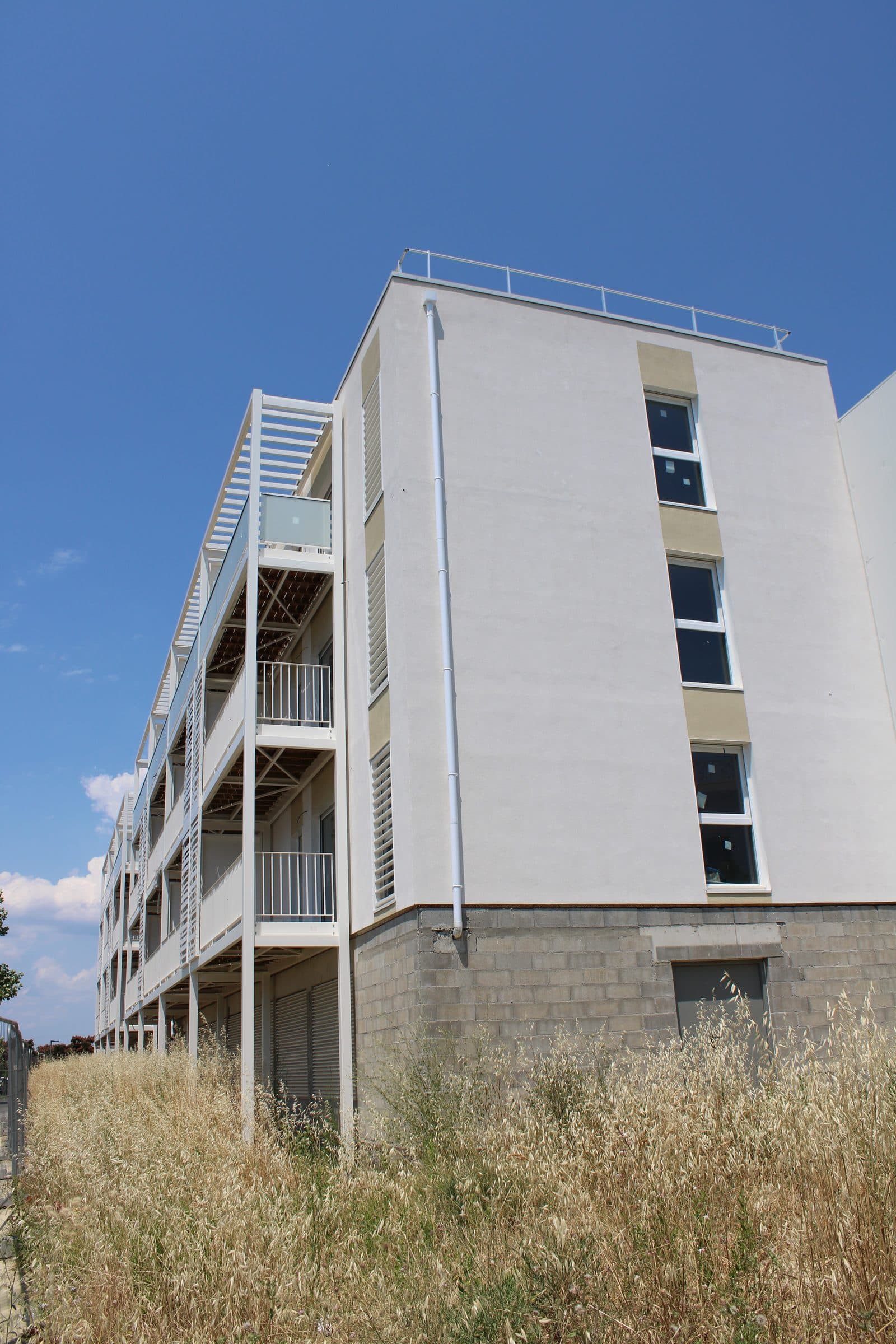 Le pignon blanc de la résidence au-dessus d’un soubassement en blocs béton